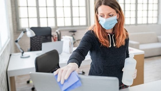 entreprise de nettoyage bureaux - une femme nettoyant l'écran d'un ordinateur dans un openspace de bureaux